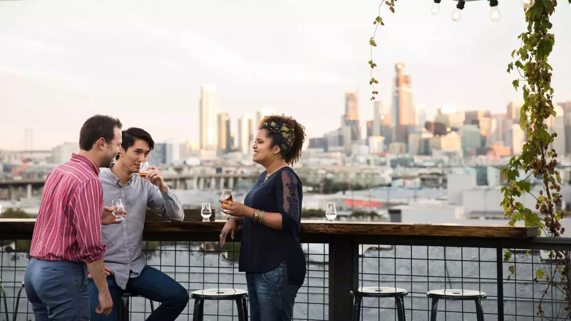 Three people gather around an outdoor table on the roof deck of Anchor Distilling in San Francisco, California.