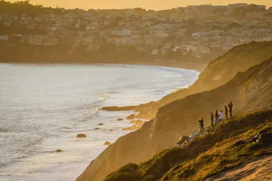 Um grupo de pessoas está à beira de um penhasco à beira-mar observando o pôr do sol no Presidio de São Francisco.